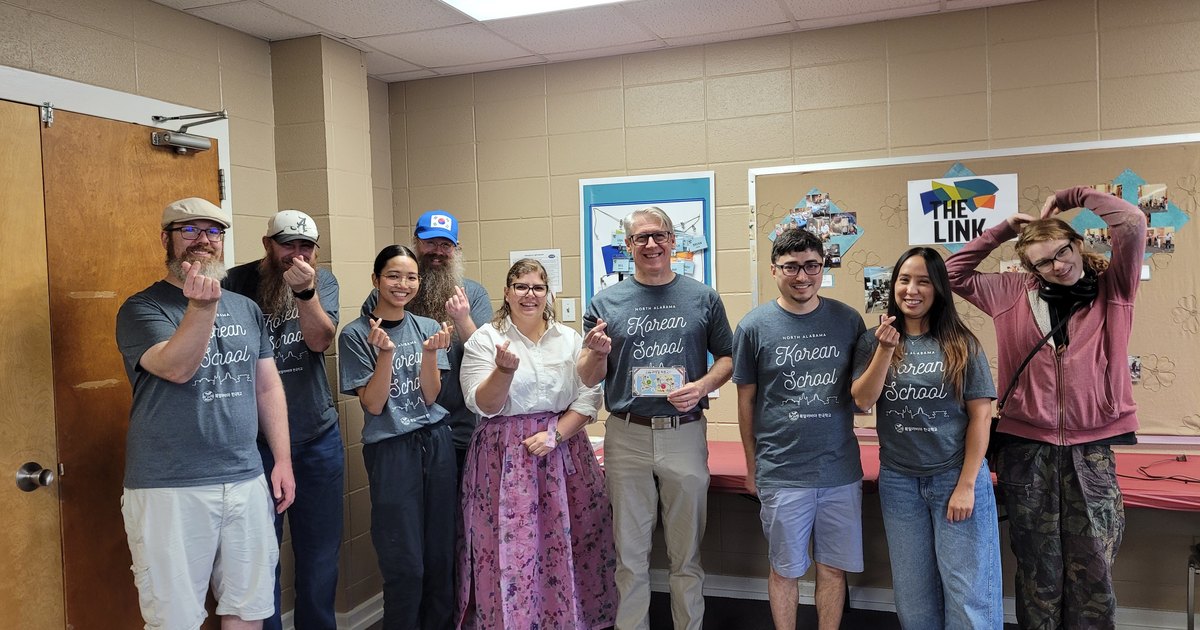 Volunteers and adult-class students in North Alabama Korean School shirts making finger hearts.